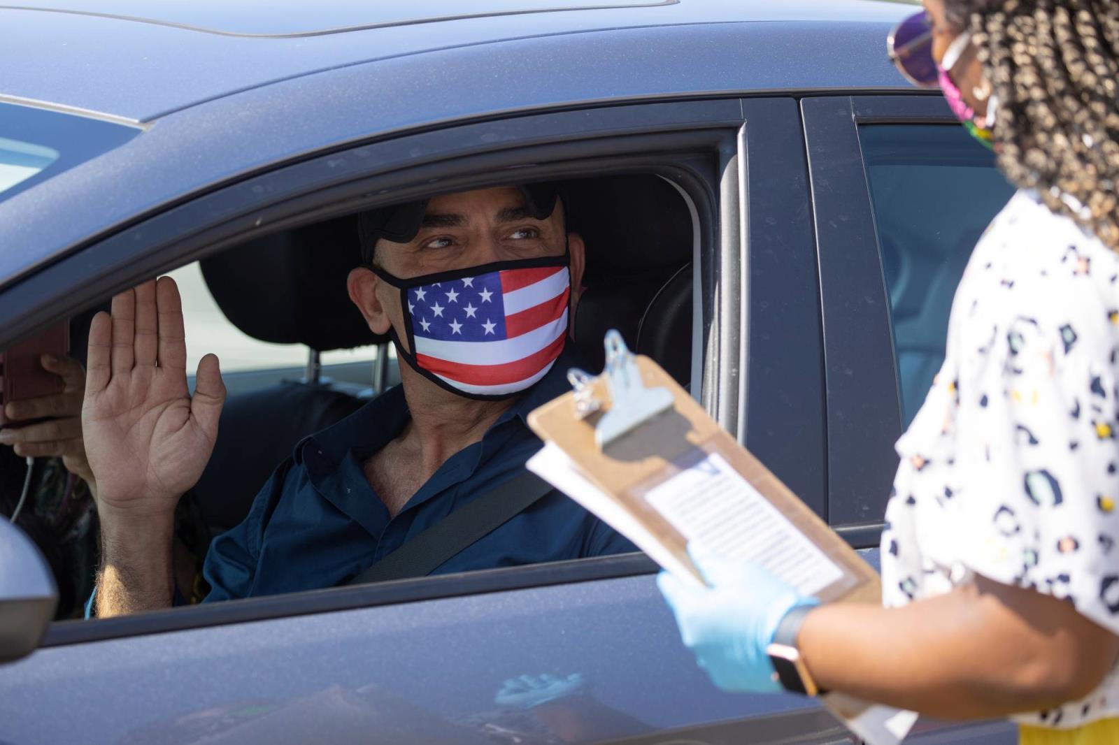 A U.S. immigration officer swears in a newly naturalized citizen in an empty parking amid the outbreak of the coro<em></em>navirus disease in Santa Ana, California, in July. |  REUTERS
