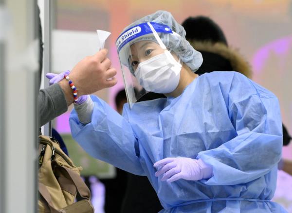 A quarantine officer checks a saliva sample from an overseas passenger as part of an antigen test for COVID-19 at Narita Airport in December. | KYODO 